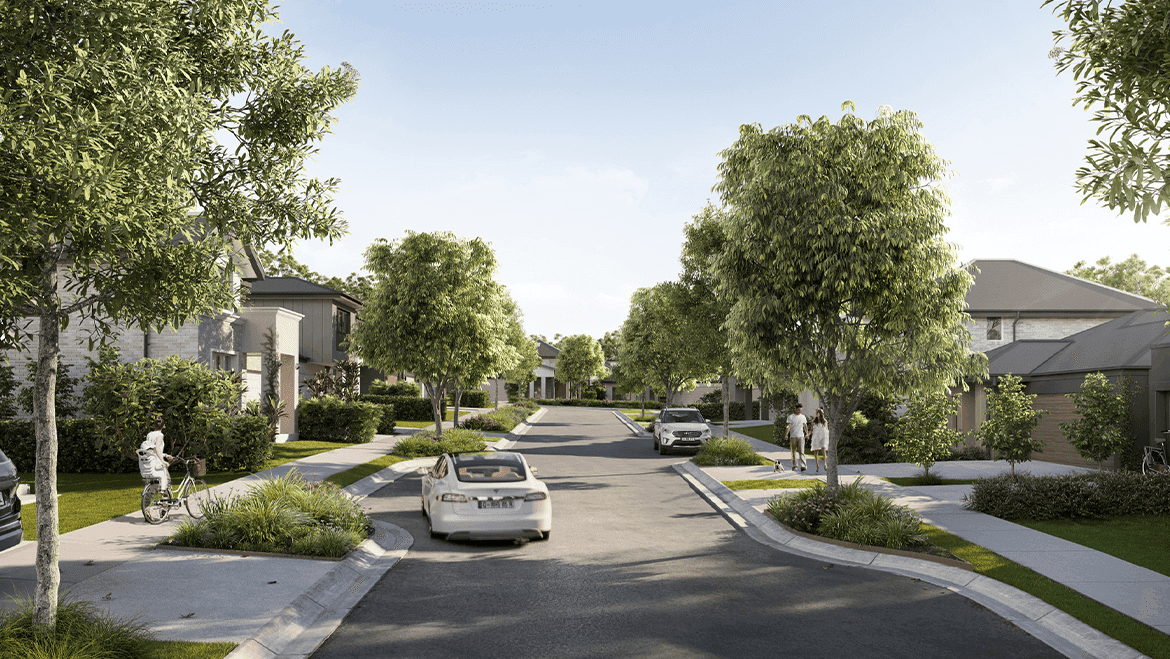 A quiet suburban street lined with green trees and modern houses. A few cars are parked along the curbs. People are walking and a cyclist rides on the sidewalk under a clear blue sky.
